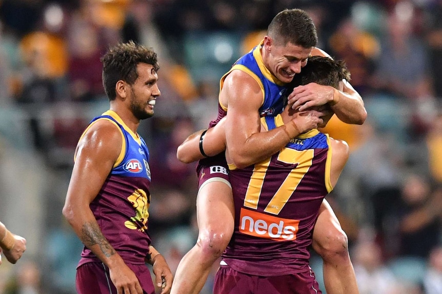 A Brisbane Lions AFL player jumps up to hug a teammate as they celebrate a goal against Collingwood.