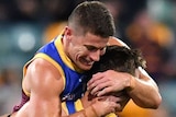 A Brisbane Lions AFL player jumps up to hug a teammate as they celebrate a goal against Collingwood.