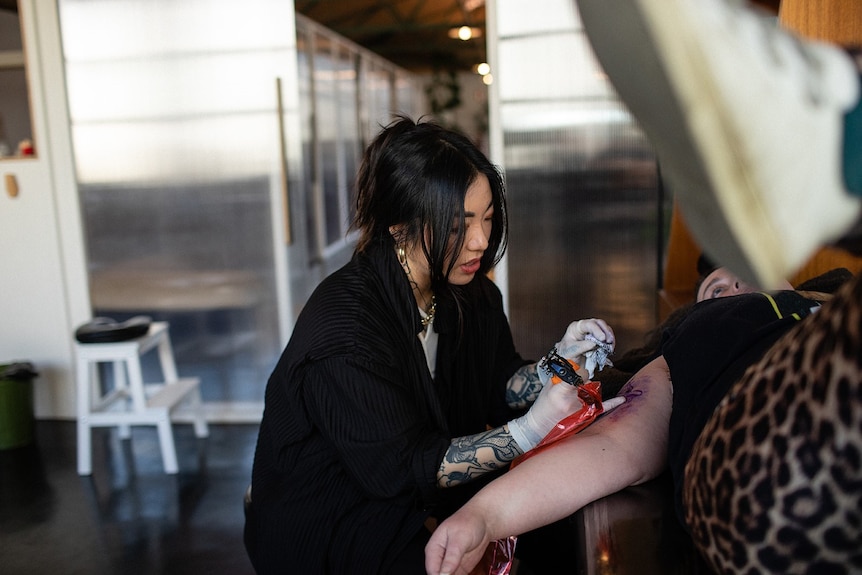 Thao Tran tattooing someones arm