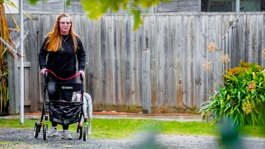 25-year-old Jasmine West walks her whippet Penny on a gravel path next to green grass and an agapanthus bush.