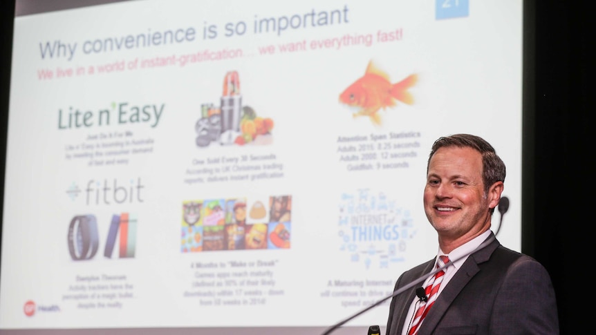 Man stands smiling at lectern with a slide showing message about convenient foods for modern consumers