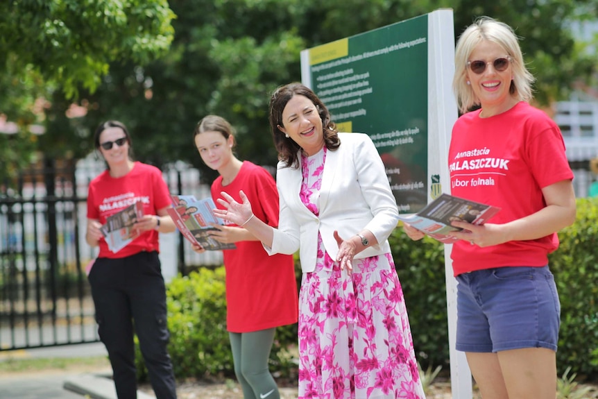 A woman smiles and waves with Labor volunteers in red shirts.