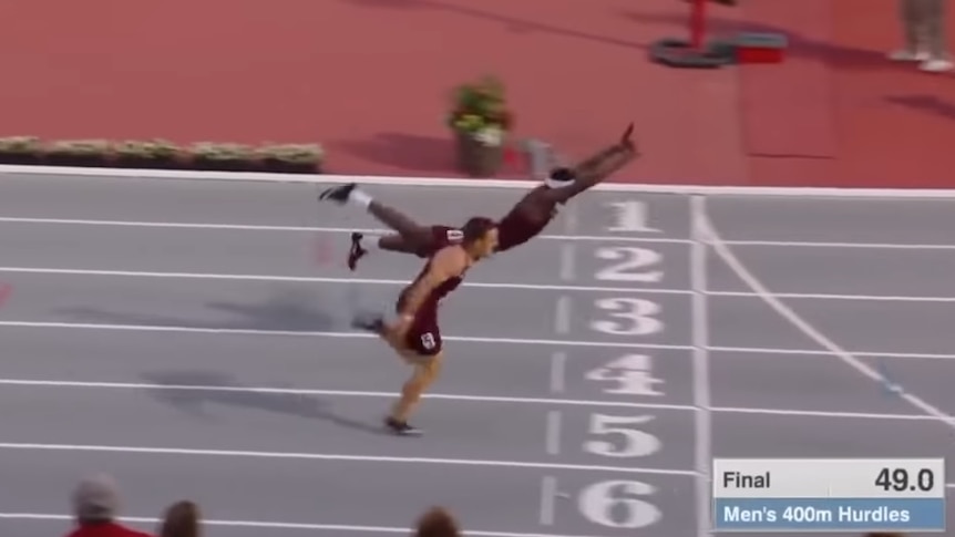 An athlete is airborne after diving full stretch to win a hurdles race inches ahead of a competitor