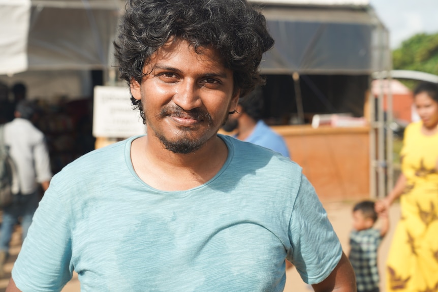 A man wearing a blue shirt and with dark hair and eyes smiles.