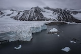 A general scene of the antarctic with ice on black rocky mountains and small ice bergs 