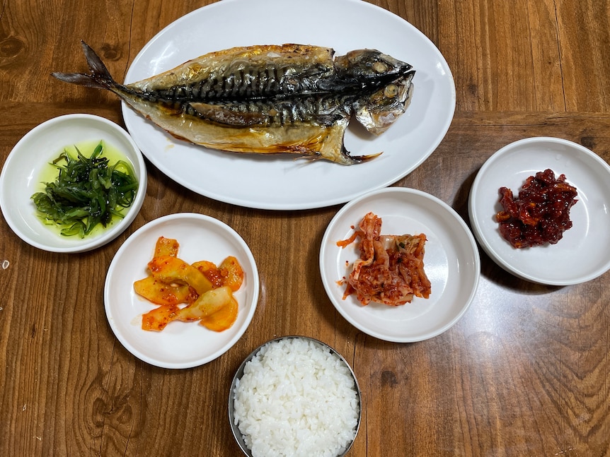 Plates on a table featuring a whole fish, rice and side dishes at a Korean restaurant.