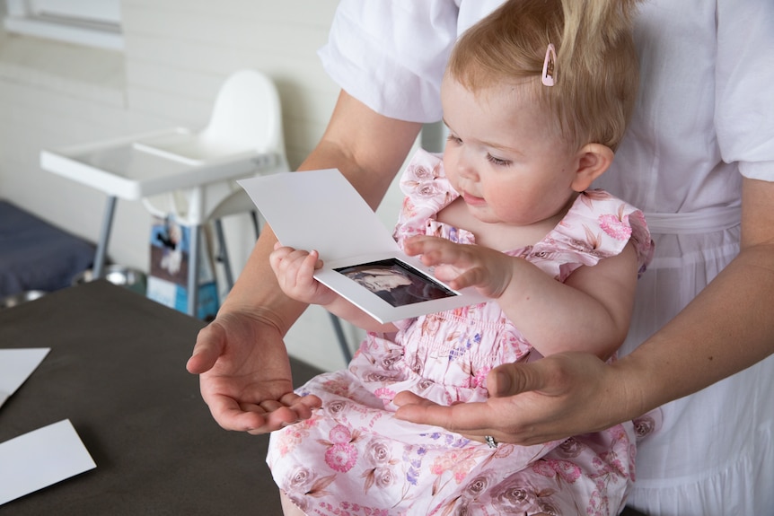 Young child looks at ultrasound image while on her mother's lap.