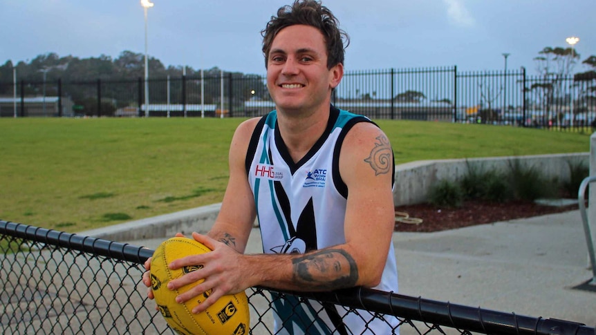 Albany Sharks footballer Jake Stuart holding a ball and leaning on a fence.