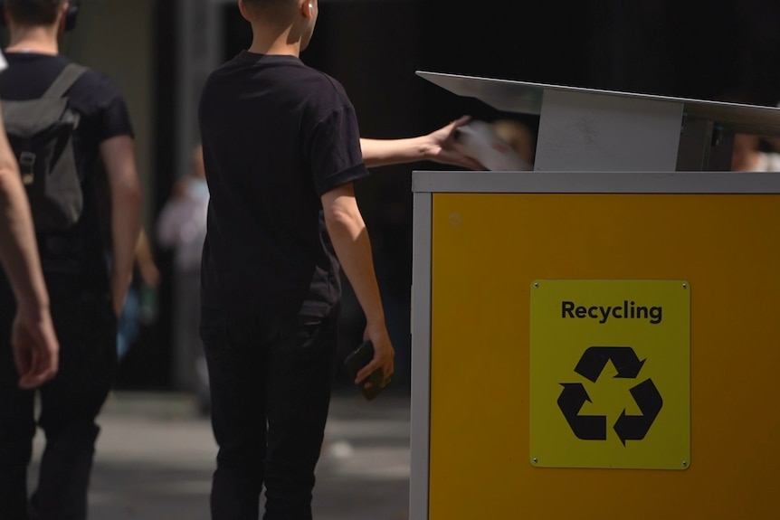 Un niño arroja algo a un contenedor de reciclaje amarillo de la ciudad.