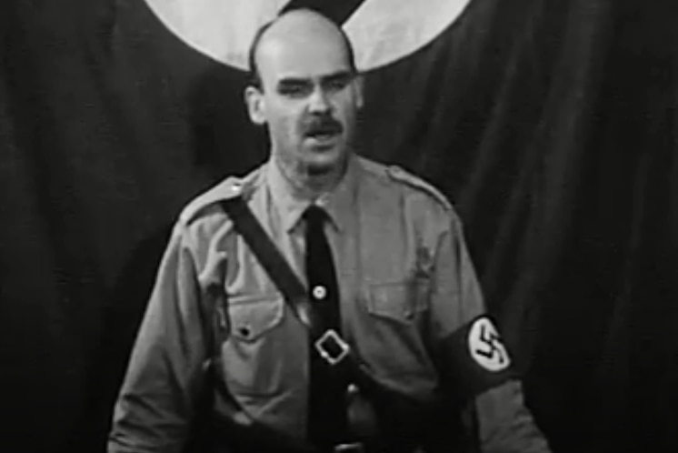A man in a khaki nazi uniform gives an address from a podium