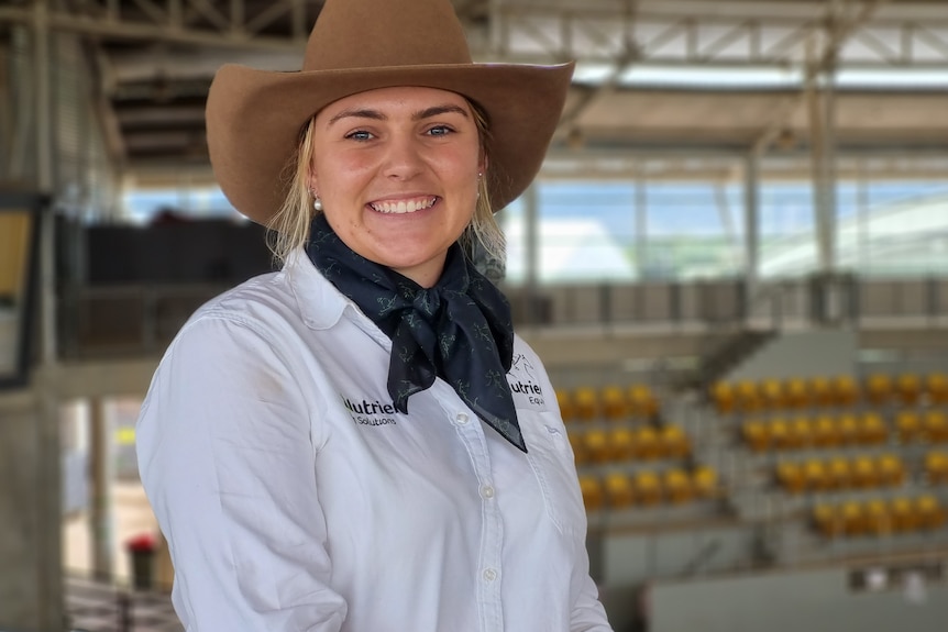 A woman in a hat and white shirts looks at the camera.