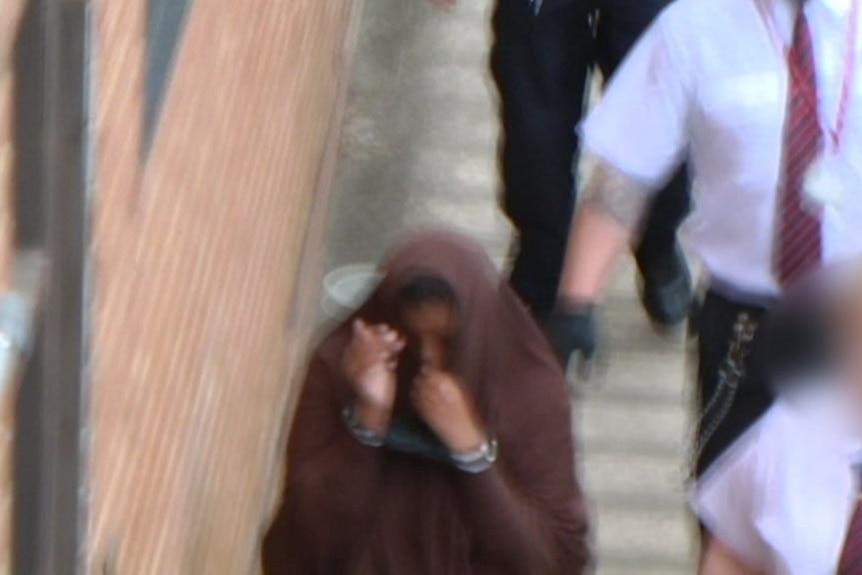 A blurred photo of a hooded woman in handcuffs.