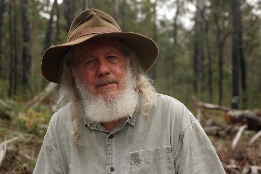A man with beard and long grey hair wearing a linen shirt and hat.