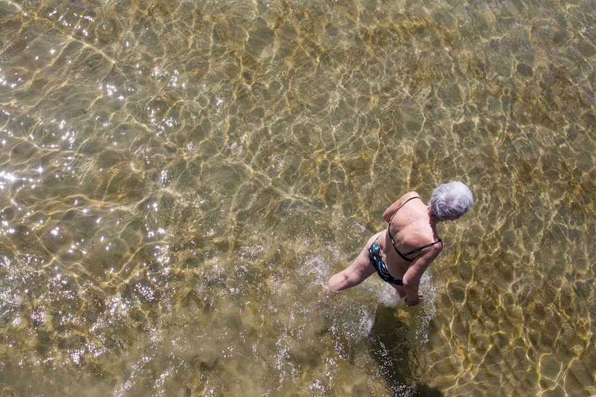 A photo looking down from a pier at a woman walking through water.