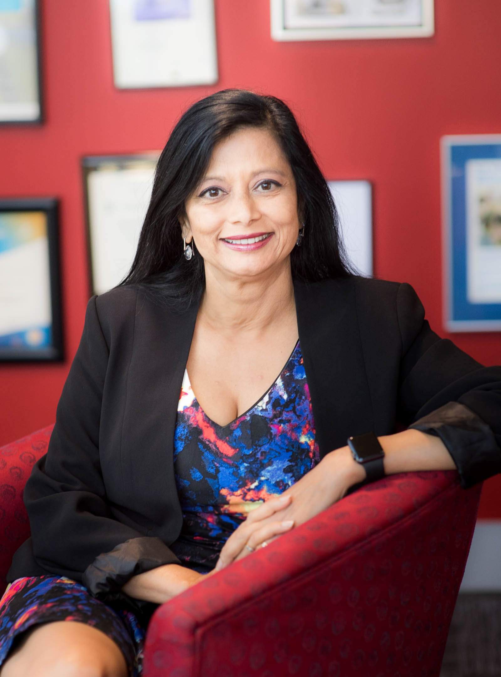 A woman with straight black hair sits in a red chair with a red office.
