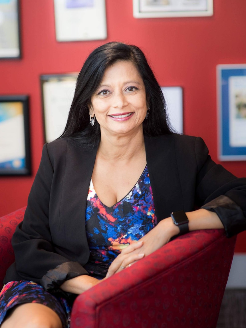 A woman with straight black hair sits in a red chair with a red office.