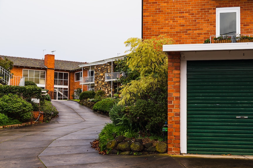 A view of a group of yellow brick homes up a concrete drive way.