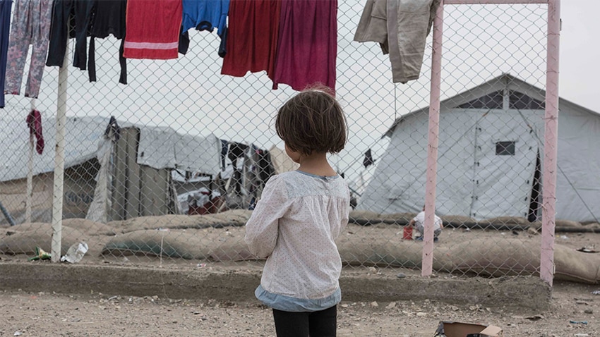 A little girl looks through a barb wire fence at the camp.