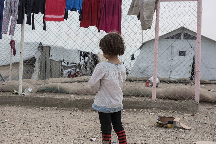 A little girl looks through a barb wire fence at the camp.