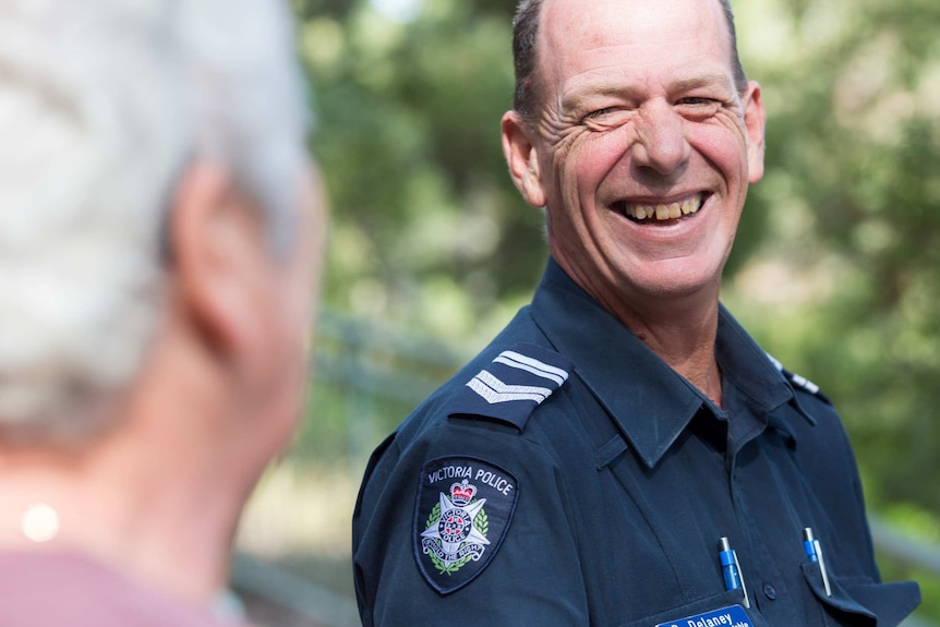 Policeman Paul Delaney laughs while talking to a tourist in a bushy setting.