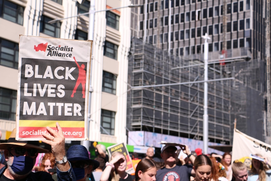 people in a crowd with a man holding up a sign reading black lives matter