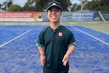 A young man with dwarfism stands on a tennis court