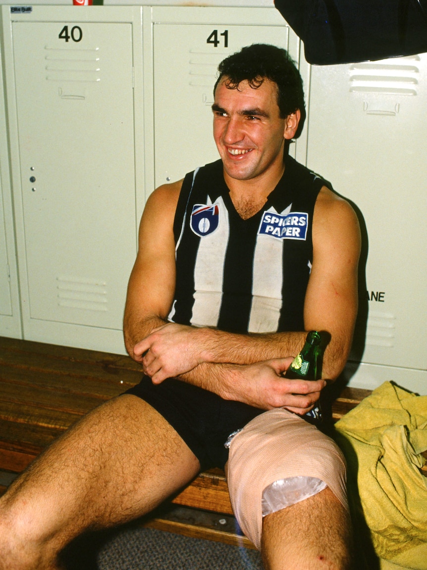 Darren Millane sits in front of lockers with a beer in his hand.