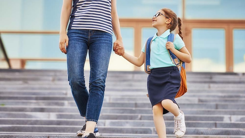 A mother and child walk to school holding hands. The child is smiling.