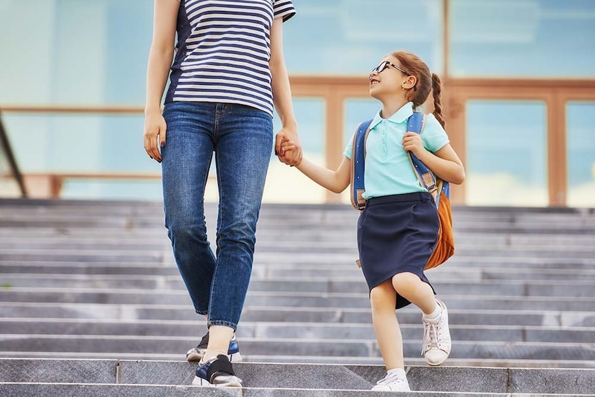 A mother and child walk to school holding hands. The child is smiling.