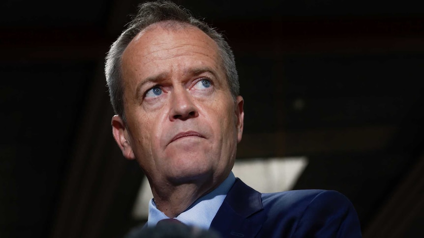 Opposition Leader Bill Shorten pauses while addressing the media in dark lighting