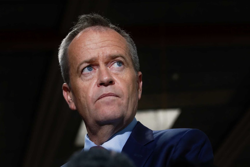 Opposition Leader Bill Shorten pauses while addressing the media in dark lighting