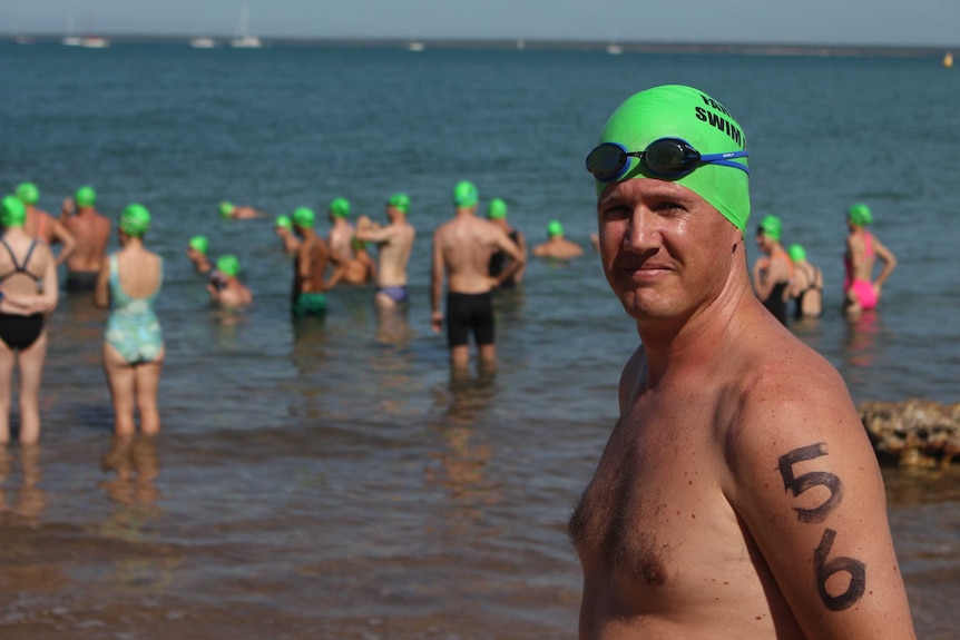 Ed Archer stands at the beach in a green swimming cap and goggles