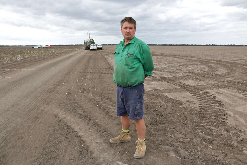 Brian Bender stands on his cotton farm, with farm equipment in the background.