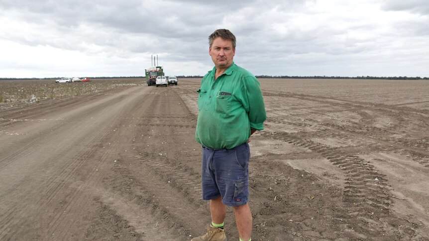 Brian Bender stands in field on his cotton farm, with farm equipment in the background.