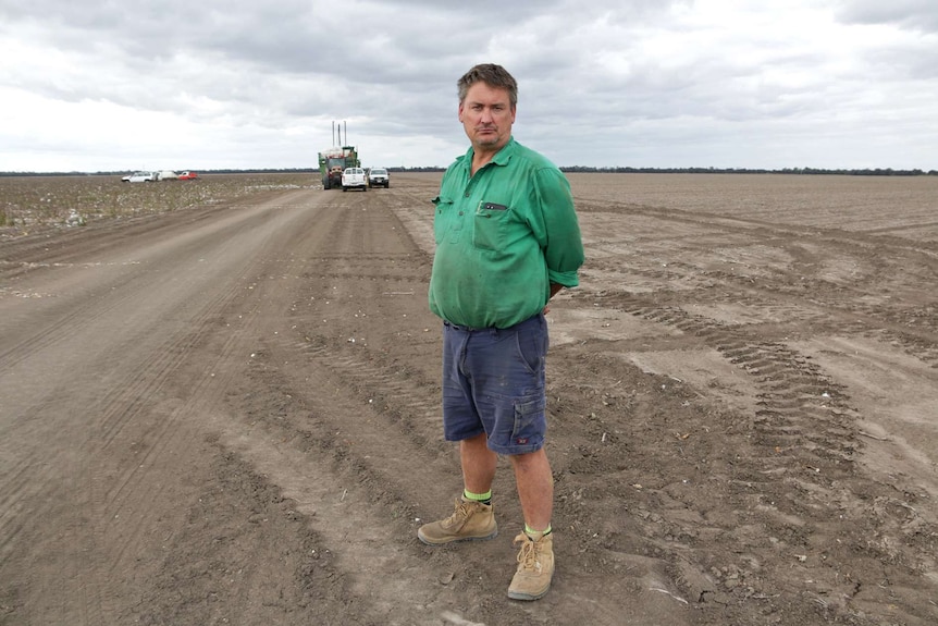 Brian Bender stands in field on his cotton farm, with farm equipment in the background.