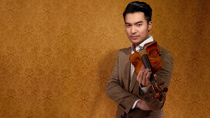 Ray Chen rest a violin on his shoulder and looks toward the camera in front of a copper textured background.