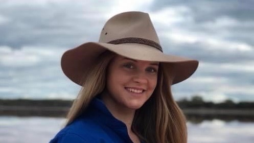 A woman in a cowboy hat smiles at the camera with a salt lake behind