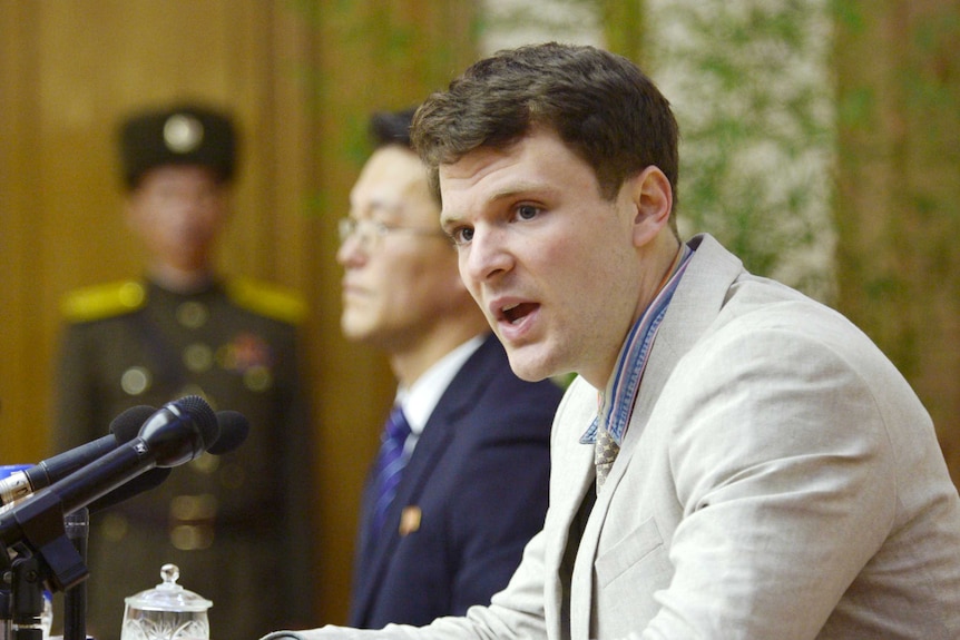 In focus: Otto Frederick sits in a beige suit speaking into several microphones.