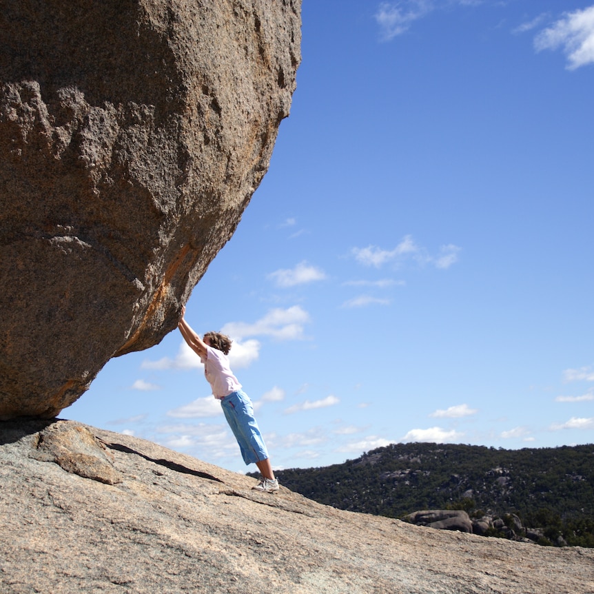 Girl pushing large rock boulder up a mountain alone