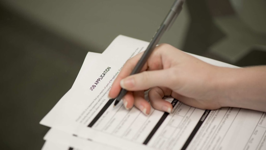 A young woman holding a pen and filling out a job application