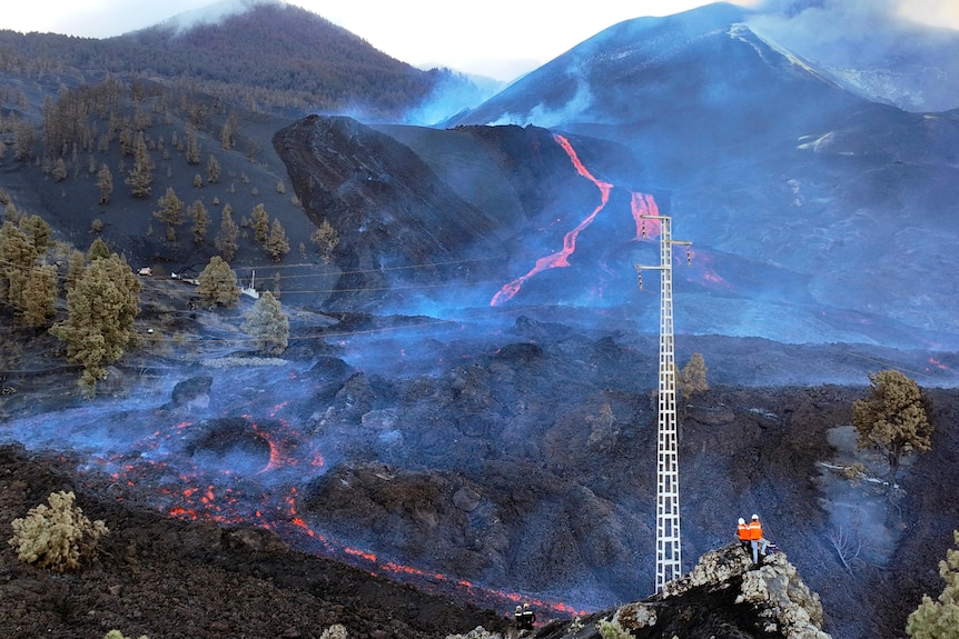 Personas con chalecos naranjas se paran en una montaña con vistas a una vulcanología.