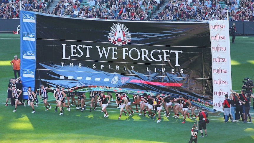 Collingwood and Essendon players run through the banner on Anzac Day at the MCG on April 25, 2016.