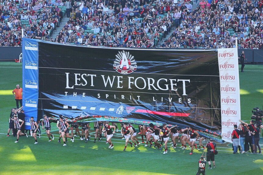 Players run through the banner for the Anzac Day match between Collingwood and Essendon at the MCG.