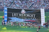 Collingwood and Essendon players run through the banner on Anzac Day at the MCG on April 25, 2016.