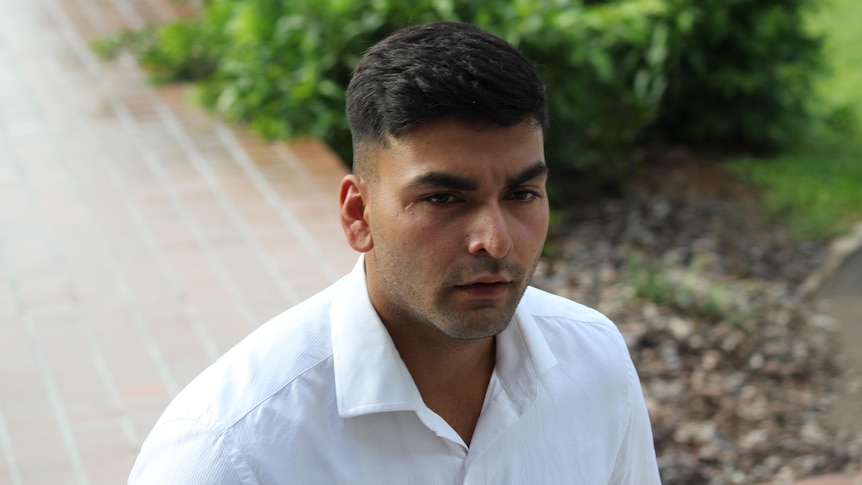 Man wearing white shirt walks along a footpath with a serious expression.