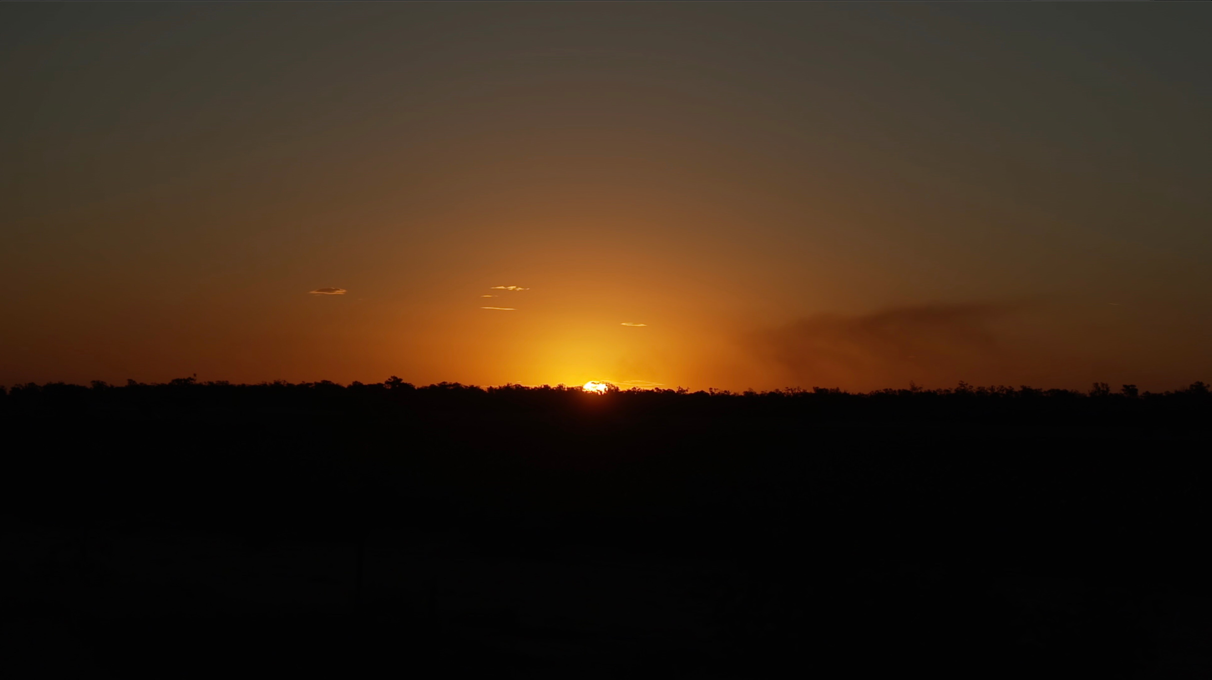 a bright red and yellow sky looks on fire. The landscape is in shadow. 
