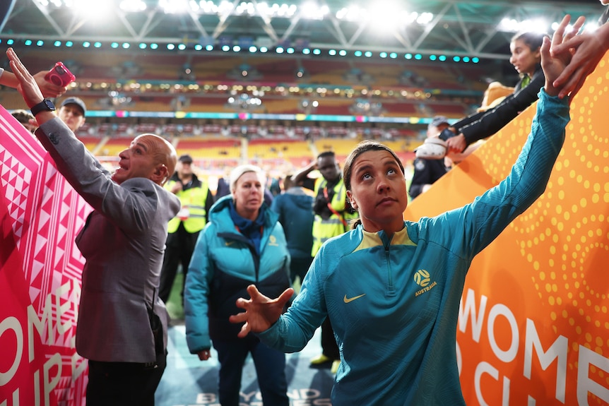 A female football player, in a tracksuit, reaches her hand to fans in a tunnel