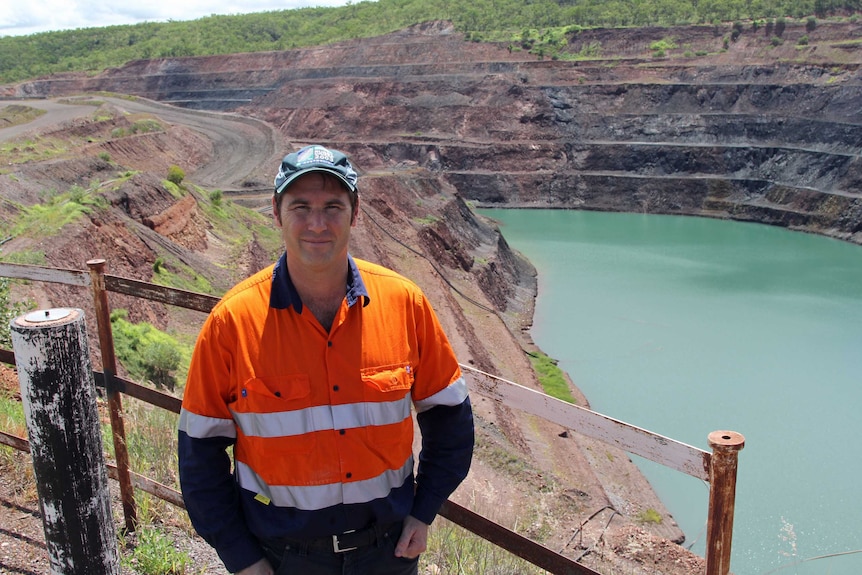 a man standing next to a large open cut mine with water in the bottom