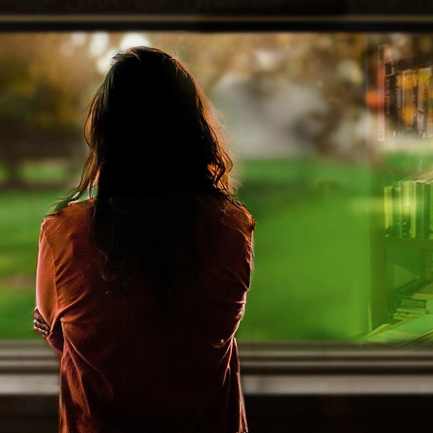 Back view of a women in silhouette, looking out of a window at green garden.