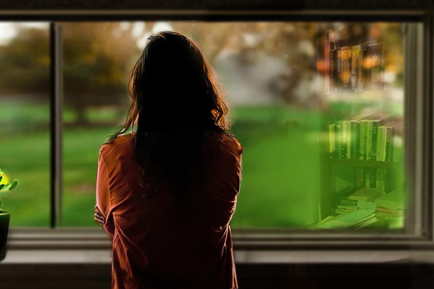 Back view of a women in silhouette, looking out of a window at green garden.